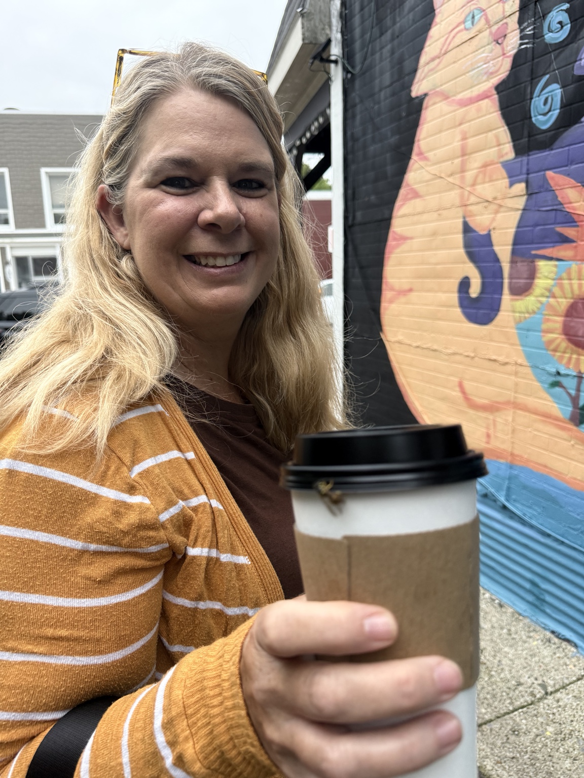 Megan enjoying coffee beside a colorful small-town mural