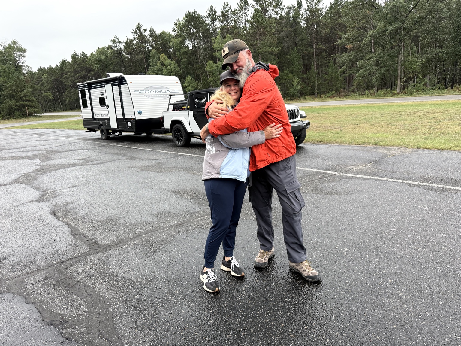 Luke and Megan hugging beside their Jeep and travel trailer