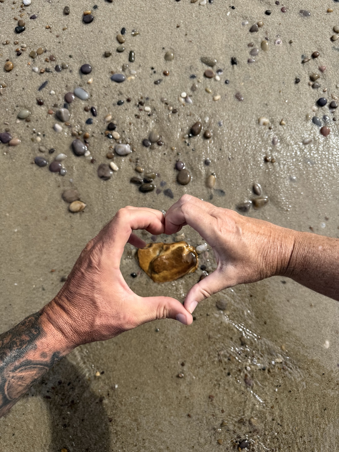Hands making a heart around a small stone found along the shore